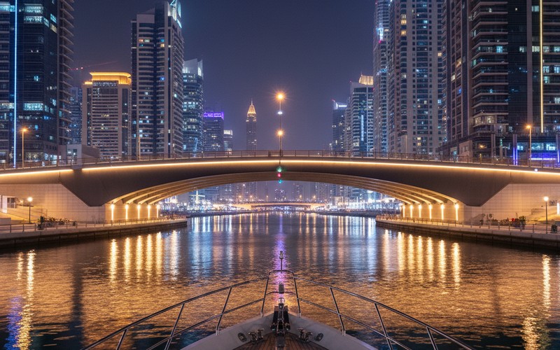 Yacht passing under illuminated Marina bridge at night